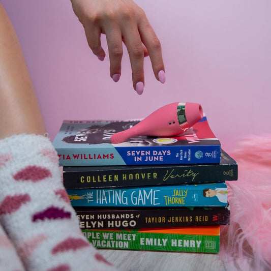 The Adventurer Vibrator laying on the side on a stack of books, hand reaching for it